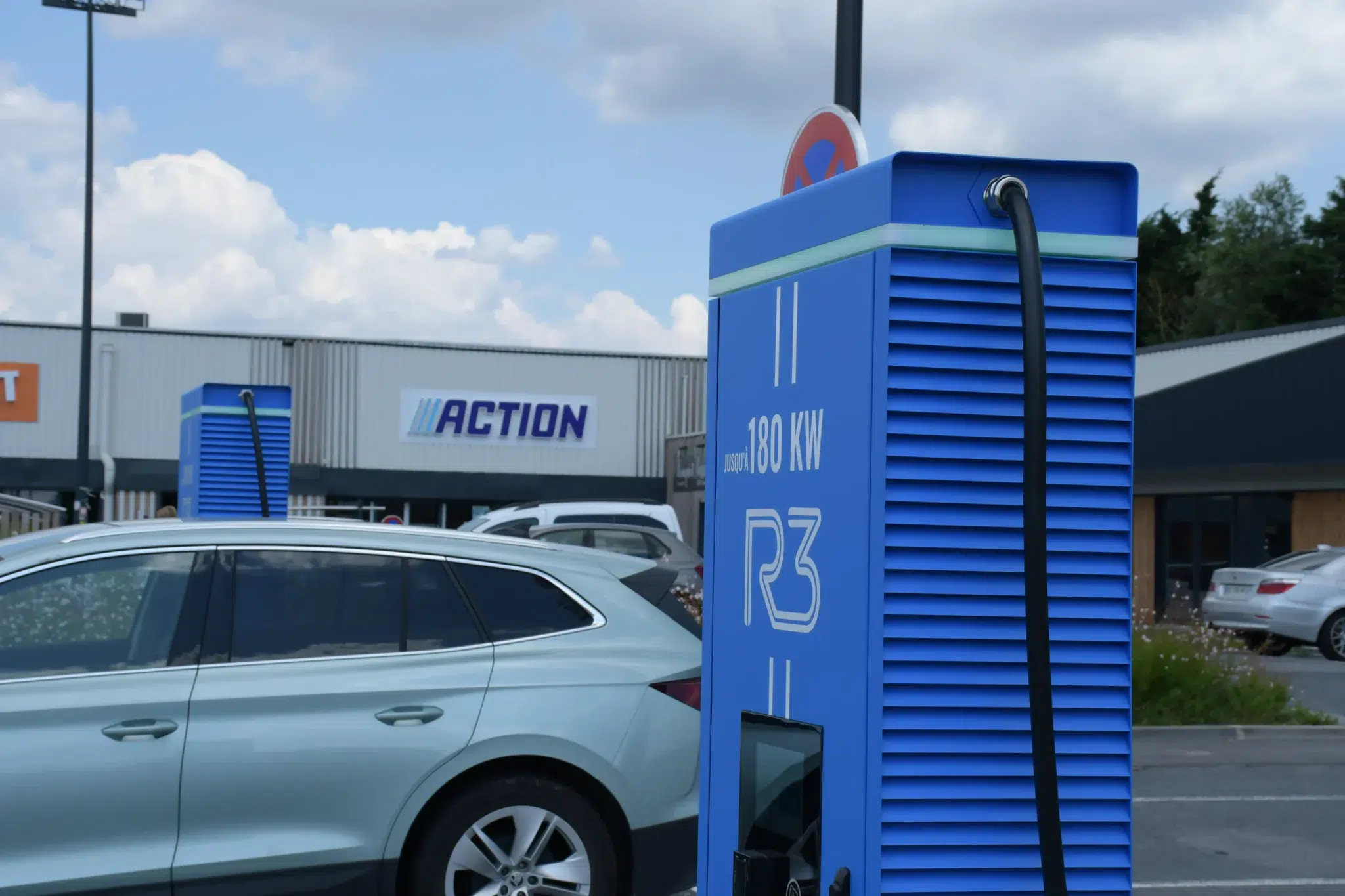 Borne de recharge rapide 180 kw pour voiture électrique installée sur un parking de centre commercial, véhicule électrique stationné en charge, infrastructure de mobilité durable facilitant la recharge lors des déplacements quotidiens.