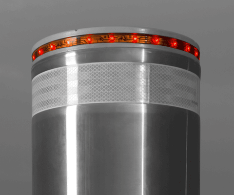 L’image montre une borne escamotable en acier inoxydable avec une finition lisse et réfléchissante. La partie supérieure de la borne est équipée d’un anneau lumineux rouge composé de LED, offrant une visibilité accrue, particulièrement utile dans des conditions de faible éclairage. Une bande réfléchissante est également visible juste en dessous de l’anneau lumineux, ajoutant une sécurité supplémentaire. Ce dispositif est conçu pour le contrôle d’accès et la sécurité des zones urbaines ou privées.